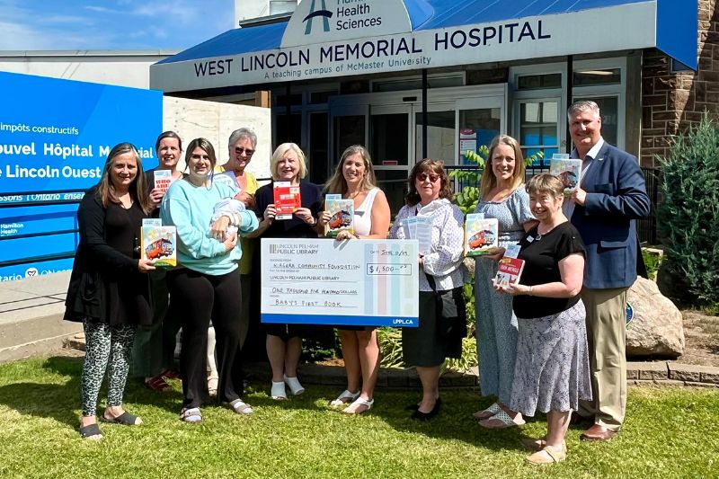 Group shot on the lawn at West Lincoln Memorial Hospital holding baby books and an oversized cheque for $1500.
