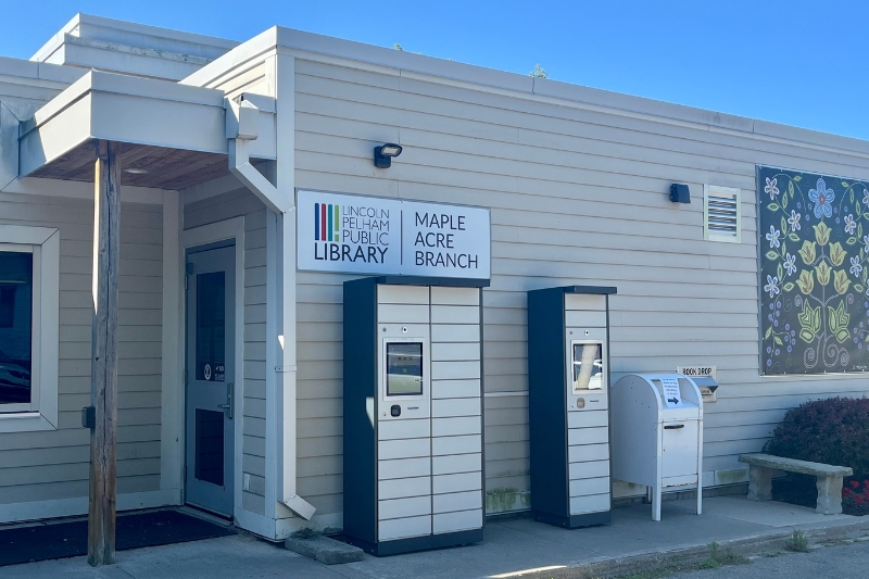 Exterior of Maple Acre library showing two book lockers, a book drop, and dot art of flowers on the back wall. 