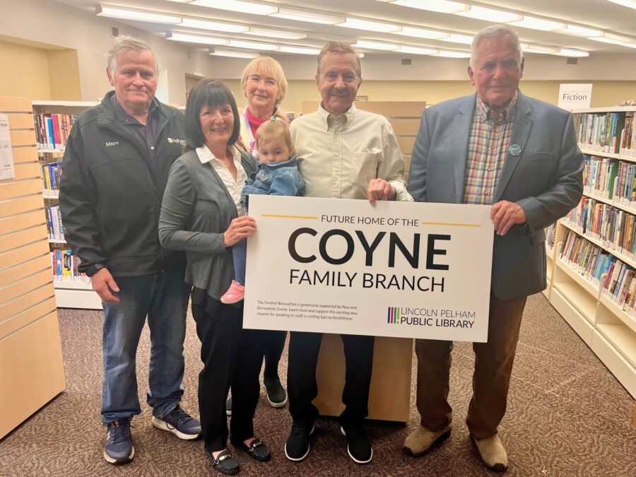 Pelham Mayor Marvin Junkin, Bernadette Coyne holding a child, Yvonne Van Lankveld, Paul Coyne, and Pelham Regional Councillor Wayne Olson holding a sigh that reads: Future Home of the Coyne Family Branch inside the Fonthill Branch.