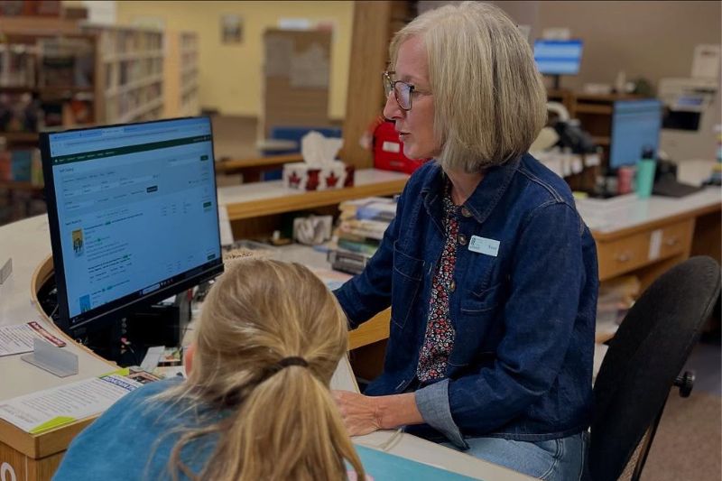 Circulation clerk Susan uses a computer to look up a book for a young girl at the Fonthill Branch service desk.